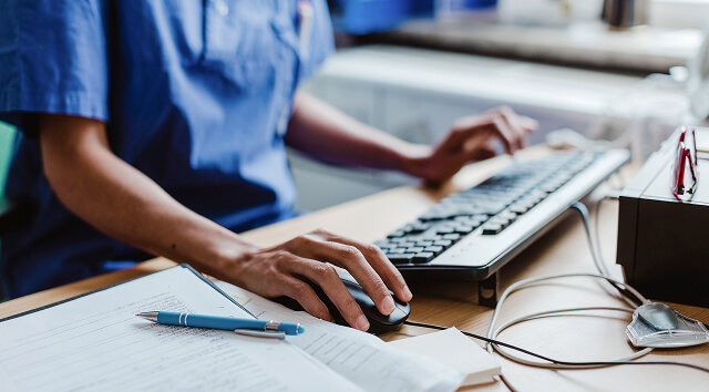 Primo piano di un professionista sanitario in camice che digita su un computer.
